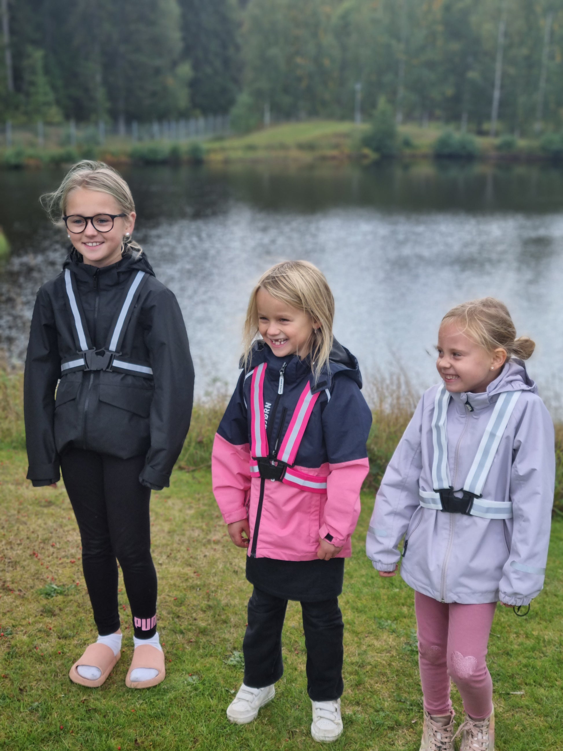 Tre glada barn med reflexselen i rosa, svart och vit kulör