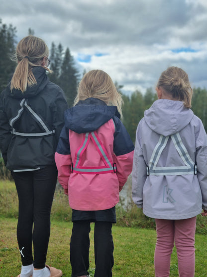 Tre glada barn med reflexselen i rosa, svart och vit kulör